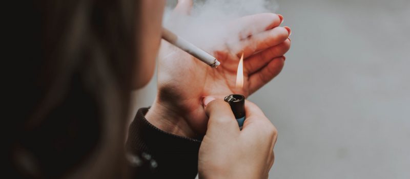 A selective closeup shot of a female lighting up a cigarette with a lighter